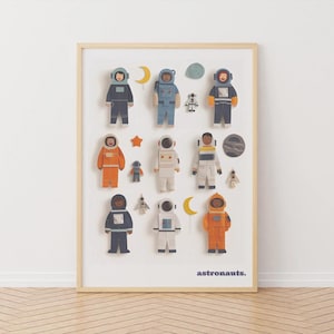 May include: A framed print with illustrations of astronauts in various suits, alongside space-themed elements. The astronauts are in different colours, with moons, stars and planets. The word "astronauts" is printed at the bottom in a simple font.