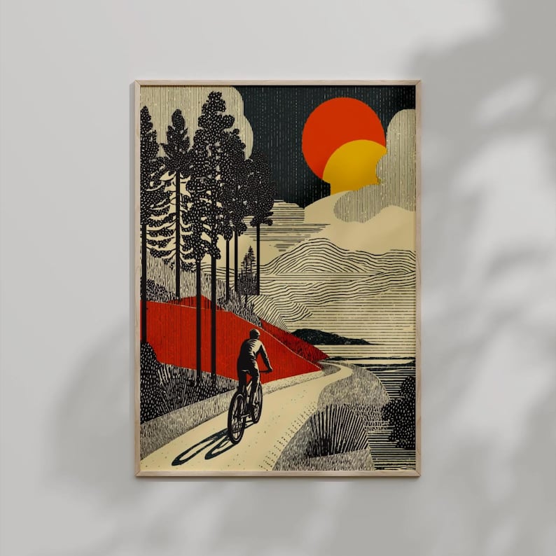May include: Framed art print featuring a cyclist on a winding road through a stylized landscape. The artwork uses a limited color palette of black, red, and yellow against a beige background. The sun is depicted as a large orange and yellow circle.
