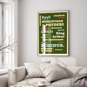 May include: A framed poster with a green background and text in various colors. The text includes names like "Pwyll," "Manawydan," and "Pryderi." The poster is hanging on a white wall above a beige sofa.