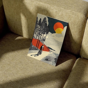 May include: A rectangular art print featuring a cyclist riding a bicycle on a mountain path. The artwork has a retro style with a red and orange sun, dark blue sky, and black and white trees. The cyclist is in silhouette.