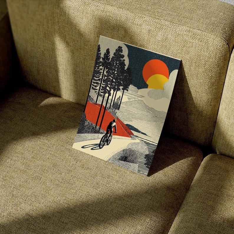 May include: A rectangular art print featuring a cyclist riding a bicycle on a mountain path. The artwork has a retro style with a red and orange sun, dark blue sky, and black and white trees. The cyclist is in silhouette.