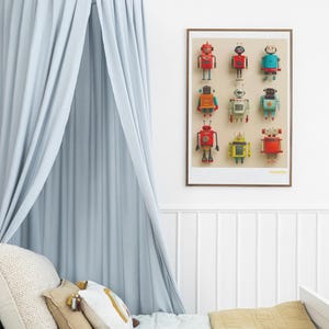 May include: A framed print featuring nine colorful robot illustrations. The robots are in various colors, including red, blue, and yellow. A light blue canopy hangs above a bed with decorative pillows and a mustard-colored blanket.