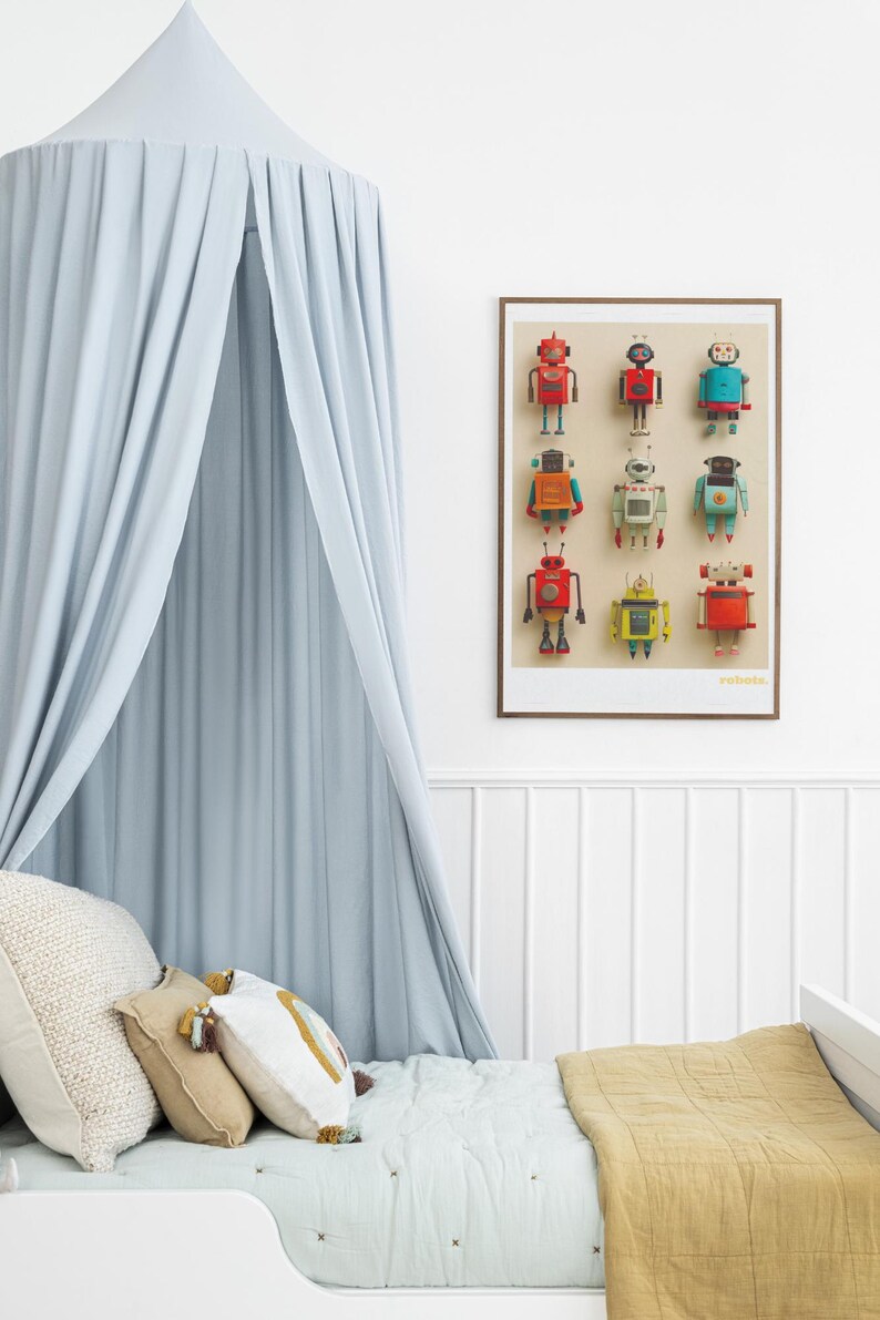 May include: A framed print featuring nine colorful robot illustrations. The robots are in various colors, including red, blue, and yellow. A light blue canopy hangs above a bed with decorative pillows and a mustard-colored blanket.