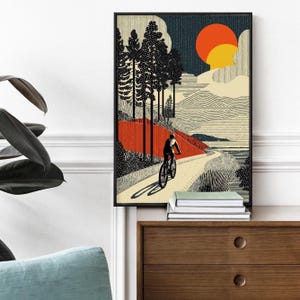 May include: Framed art print featuring a cyclist on a winding path through a landscape. The artwork showcases a stylized illustration with a red and orange sun, tall trees, and a textured sky. The print is in a black frame.