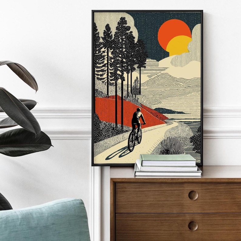 May include: Framed art print featuring a cyclist on a winding path through a landscape. The artwork showcases a stylized illustration with a red and orange sun, tall trees, and a textured sky. The print is in a black frame.