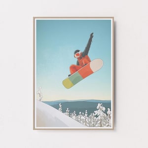 Puede incluir: Una impresión enmarcada que presenta a un snowboarder en el aire contra un cielo azul. El snowboarder lleva un atuendo naranja y negro y un casco. La tabla de snowboard es multicolor, con secciones de naranja, verde y crema. Hay árboles y montañas cubiertas de nieve en el fondo.