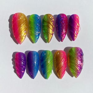 May include: A set of ten artificial nails in various colors. The nails feature a gradient effect with glitter and swirl designs. Colors include gold, pink, green, blue, and purple. The nails are oval-shaped and have a glossy finish.