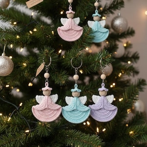 May include: Crocheted angel ornaments in pastel pink, blue, and lavender hang on a Christmas tree. Each angel has a halo, wings, and a wooden bead accent. The ornaments are attached to keychains.