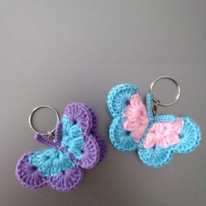 May include: Two handmade crochet butterfly keyrings. One butterfly has purple and blue wings, the other has pink and blue wings. Each keyring has a silver metal ring attached for keys or accessories. The butterflies are made with a textured stitch.