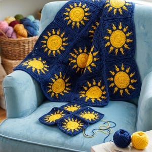 May include: A handmade crochet blanket with a repeating sunburst pattern in navy blue and yellow. The blanket is draped over a light blue armchair, with additional squares and yarn visible. A cozy, handcrafted home decor item.