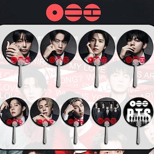 May include: A collection of eight hand fans featuring images of a musical group. Each fan has a silver handle and a circular design with a portrait of a band member. The fans have red and white accents and the band's logo.