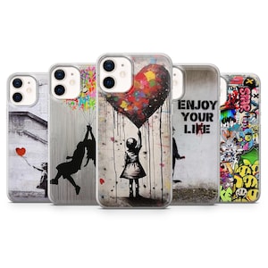 Puede incluir: Un conjunto de fundas para teléfonos con diseños de arte callejero. Las fundas muestran varias obras de arte, incluyendo una niña sosteniendo un globo en forma de corazón, una niña columpiándose de globos y graffiti con el texto "ENJOY YOUR LIFE".