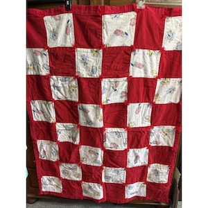 May include: A rag quilt featuring a checkerboard pattern of solid red fabric squares and white fabric squares printed with small illustrations of teddy bears in various outfits. The squares are joined with exposed frayed red seams.