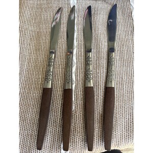 May include: Four vintage stainless steel knives with brown wooden handles. The blades are silver and the handles are a dark brown color. The knives have a decorative silver design on the handle near the blade.