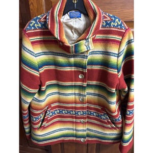 May include: A Pendleton jacket featuring a vibrant horizontal striped pattern in shades of red, yellow, green, and blue. The jacket has a high collar, a button-front closure with metallic buttons, two side pockets, and a light-colored interior lining.