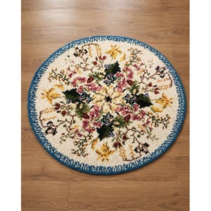 May include: A round rug with a cream-colored background featuring a central floral pattern in shades of pink, yellow, green, and dark red. The rug is finished with a distinct blue border that frames the intricate botanical design throughout the piece.