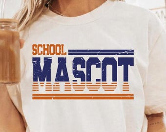 Puede incluir: Camiseta de color marfil con las palabras "SCHOOL MASCOT" en letras de bloque naranja y azul. El diseño incluye rayas horizontales naranjas debajo de la palabra "MASCOT". La camiseta está hecha de un material suave.