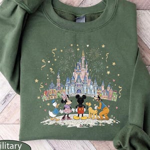 A green sweatshirt with a Disney-themed illustration of Minnie Mouse, Donald Duck, and Goofy standing in front of a castle, with fireworks in the background.