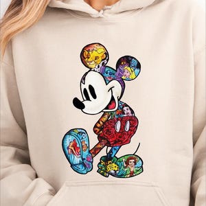 A woman wearing a beige hoodie with a colorful, cartoon-style illustration of Mickey Mouse printed on it.