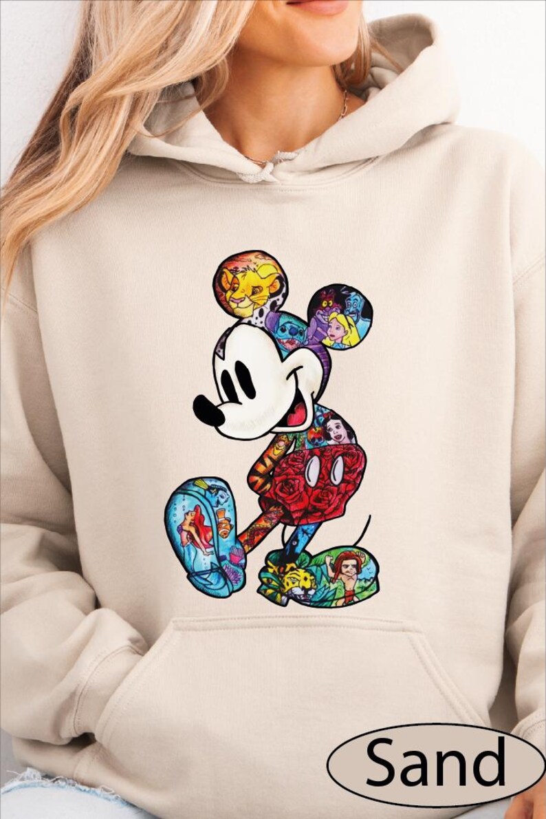 A woman wearing a beige hoodie with a colorful, cartoon-style illustration of Mickey Mouse printed on it.