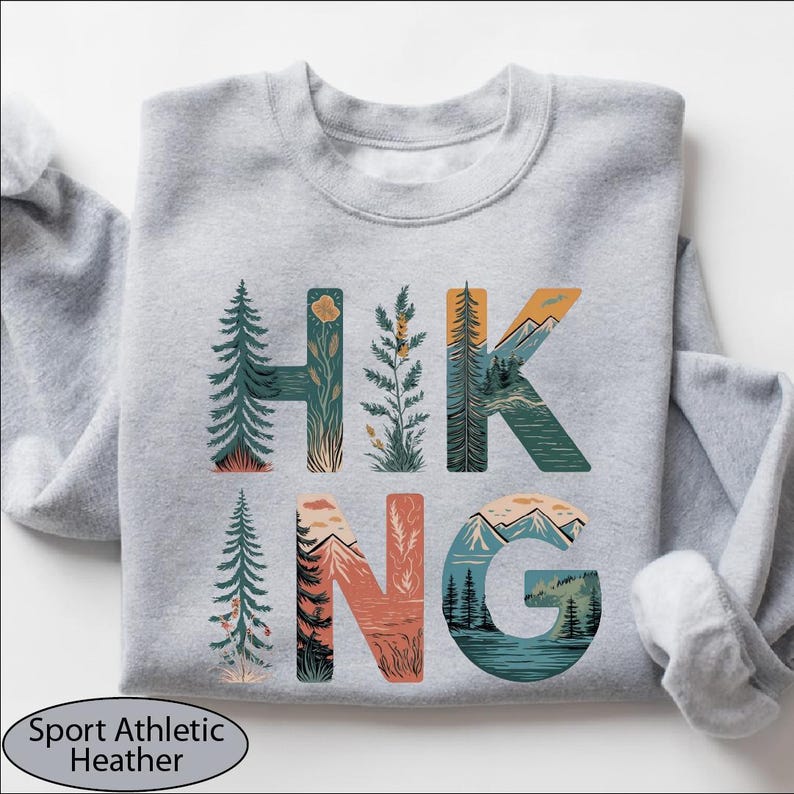 A gray sweatshirt with the word "HIKING" printed on it, featuring various nature-inspired illustrations such as pine trees, mountains, and forests.