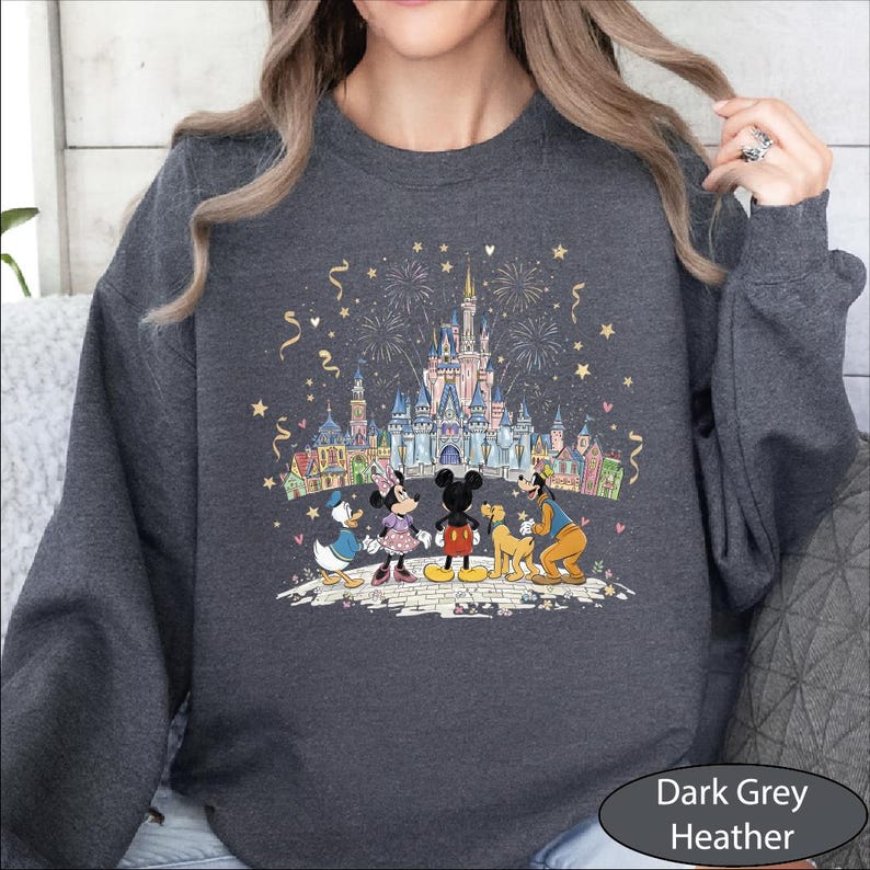 A woman wearing a gray sweatshirt with a colorful illustration of Disney characters and a castle on a fireworks display.