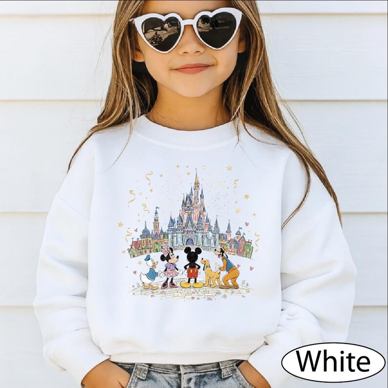 A young girl wearing a white sweater with a Disney castle and characters printed on it, smiling and posing for the camera.