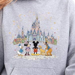 A gray hoodie with a graphic design featuring Disney characters Mickey Mouse, Minnie Mouse, Goofy, and Donald Duck standing in front of a castle.