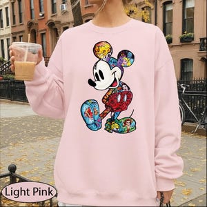 A person wearing a pink sweatshirt with a colorful, cartoon-style illustration of Mickey Mouse printed on it.