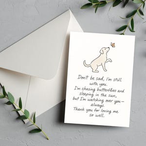 May include: A white greeting card with a dog illustration and a butterfly, accompanied by a white envelope. The card features the text: "Don't be sad, I'm still with you..." A heartfelt sympathy card.