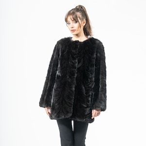 Könnte beinhalten: Ein schwarzer Kunstfellmantel mit rundem Ausschnitt und langen Ärmeln. Der Mantel hat ein strukturiertes Muster und wird mit einer schwarzen Hose und schwarzen Absätzen getragen. Der Hintergrund ist weiß.