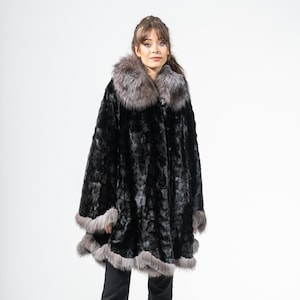 Könnte beinhalten: Ein schwarzer Pelzmantel mit grauem Pelzkragen und -besatz. Der Mantel hat ein strukturiertes Muster und wird mit schwarzer Hose und schwarzen Absätzen getragen. Das Model steht vor einem weißen Hintergrund.