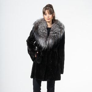May include: A black fur coat with a silver and grey fur collar. The coat has a belt at the waist and is worn with black trousers. The coat is a luxurious outerwear garment.