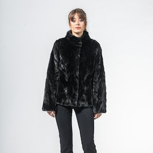 Puede incluir: Chaqueta negra de piel sintética con cuello alto y mangas largas. La chaqueta está abotonada y se lleva con pantalones negros y tacones negros de punta. El fondo es blanco.