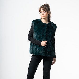 Op de afbeelding: Een donkergroen imitatiebont vest met een textuurpatroon. Het vest wordt gedragen over een zwart shirt met lange mouwen en gecombineerd met een zwarte broek. Het model draagt zwarte hakken.