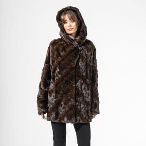 Peut inclure: Un manteau à capuche marron avec un motif texturé. Le manteau a une fermeture à bouton et est porté avec un pantalon noir et des chaussures noires. Le manteau semble être en fausse fourrure.