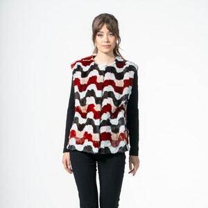 May include: A woman wearing a colorful faux fur vest with a wavy pattern in red, white, brown, and black. She is also wearing a black long-sleeve shirt, black pants, and black shoes. The vest is the focal point of the image.