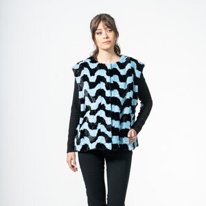 Puede incluir: Un chaleco sin mangas con un estampado de zigzag negro y azul claro. El chaleco se lleva sobre una camisa negra de manga larga y se combina con pantalones negros. El conjunto se completa con zapatos negros. El chaleco es una pieza llamativa.