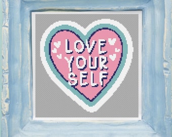 Puede incluir: Un bordado enmarcado con las palabras "LOVE YOUR SELF" en blanco sobre un corazón rosa. El corazón tiene un contorno turquesa y está sobre un fondo gris. El marco es de color azul claro.