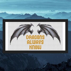 May include: Cross stitch pattern featuring a pair of gray dragon wings with the text "DRAGONS ALWAYS KNOW" in yellow.