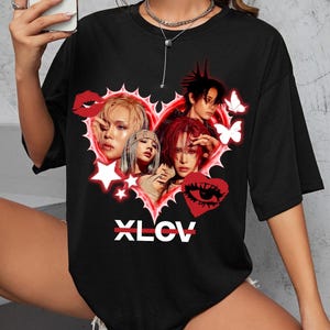 May include: Black crew neck t-shirt featuring a heart-shaped graphic with four faces, butterflies, stars, and lips. The graphic is outlined in red and includes the text "XLCV" in white.