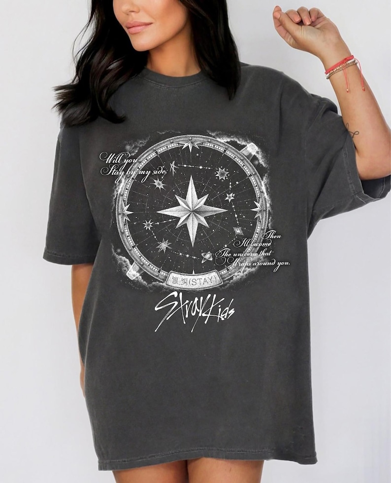 Peut inclure: T-shirt gris fonc&eacute; avec un motif de boussole, une &eacute;toile centrale et le texte "Will you stay by my side, then the universe that wraps around you." Le t-shirt porte &eacute;galement l'inscription "Stray Kids".