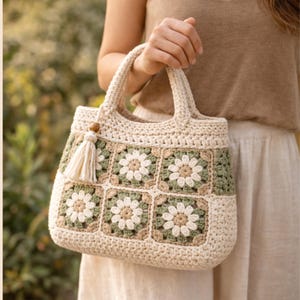Puede incluir: Bolso tote de crochet color crema con un patr&oacute;n floral en verde, beige y blanco. El bolso presenta un detalle de borla y cuentas de madera. Las asas son resistentes y el bolso parece hecho a mano.