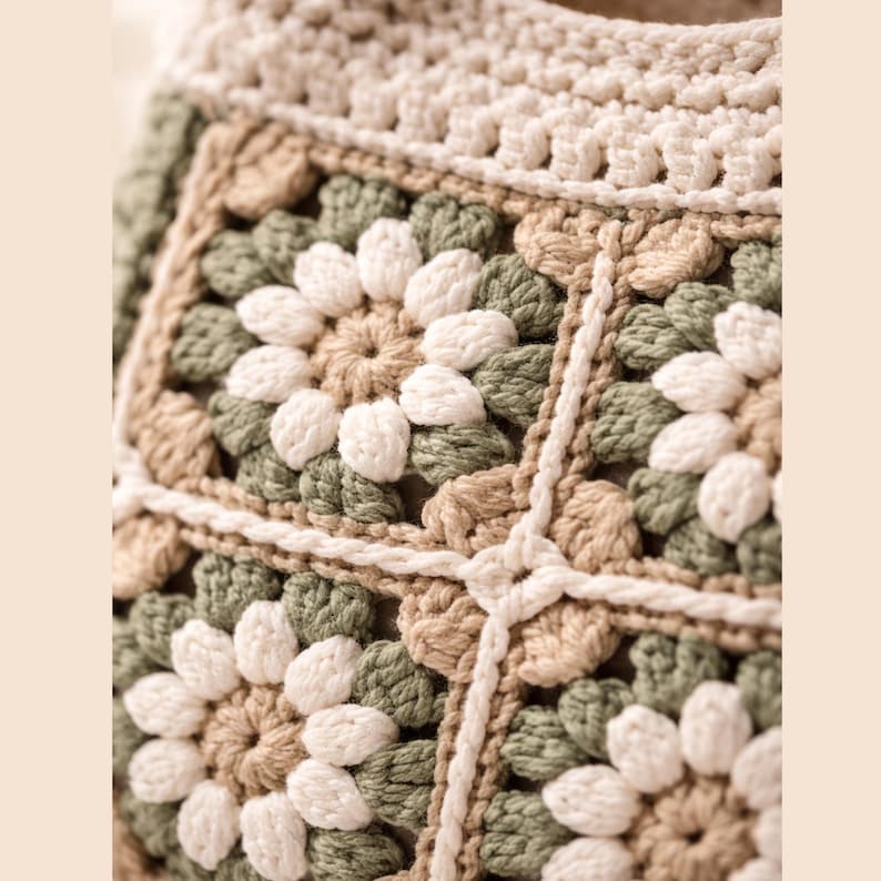 Puede incluir: Primer plano de un bolso de ganchillo con un estampado floral. El bolso presenta un dise&ntilde;o de cuadrados de la abuela en tonos crema, verde y marr&oacute;n. Las puntadas de ganchillo son visibles, creando una superficie texturizada. El borde superior del bolso es de color crema liso.