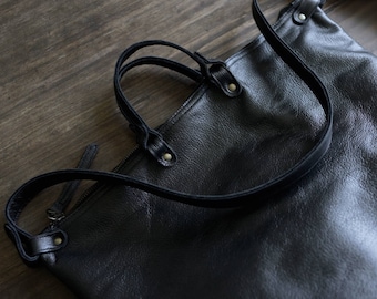 May include: A black leather tote bag with a long strap. The bag has a zipper closure and a top handle.