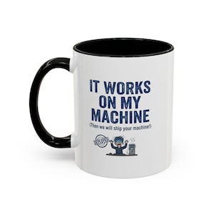 May include: A white ceramic mug with a black handle and interior. The front features blue text that reads IT WORKS ON MY MACHINE (Then we will ship your machine!) above a graphic of a stressed person at a computer with a DEPLOYED stamp.