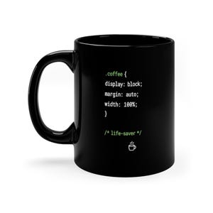 May include: A black ceramic mug featuring white and light green CSS code text that reads .coffee { display: block; margin: auto; width: 100%; } followed by a comment /* life-saver */ and a small white line-art icon of a coffee cup.