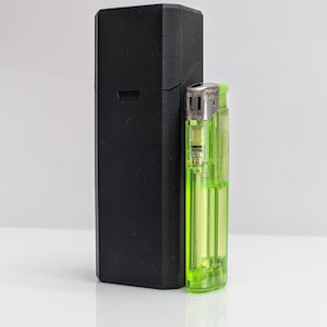 Puede incluir: Una funda rectangular negra est&aacute; junto a un encendedor verde transparente. La funda es alta y tiene un acabado mate. El encendedor es de tama&ntilde;o est&aacute;ndar, con una parte superior de metal y una c&aacute;mara de combustible visible.