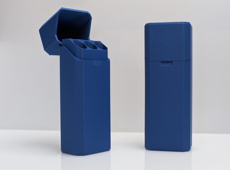 Puede incluir: Dos estuches rectangulares azul cobalto. Un estuche est&aacute; abierto, revelando tres compartimentos cil&iacute;ndricos. El otro estuche est&aacute; cerrado. Ambos estuches tienen una superficie texturizada y un dise&ntilde;o geom&eacute;trico. Los estuches est&aacute;n sobre una superficie blanca.