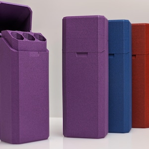 Puede incluir: Una colecci&oacute;n de estuches rectangulares en varios colores: morado, azul, rojo y negro. El estuche morado est&aacute; abierto, revelando tres compartimentos cil&iacute;ndricos. Los estuches tienen una superficie texturizada y un dise&ntilde;o geom&eacute;trico.